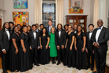 A group dressed in formal attire pose for a photo with a woman in a green suiting dress.