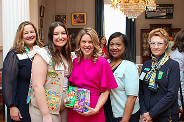 The First Lady poses holding Girl Scout cookies with a group of women and a Girl Scout inside the Mansion.
